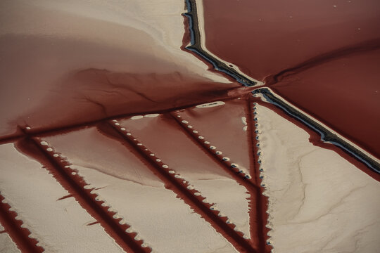 Aerial view of the Great Salt Lake showing vibrant red water contrasting with white salt flats and geometric patterns of dikes and channels in Salt Lake City, Utah, United States.