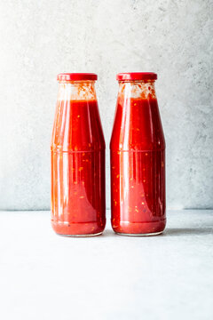 Two glass bottles sealed with red caps hold red Tomato sauce