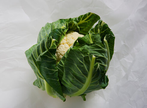 Fresh cauliflower head with green leaves on white background