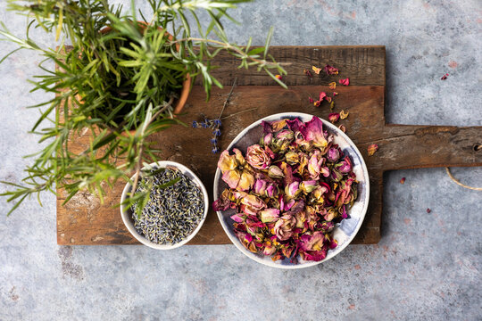 Dried rose petals and lavender with potted rosemary on a cutting board
