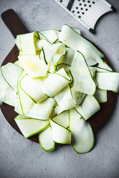 Sliced Zucchini strips on wooden cutting board with kitchen grater