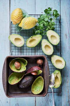 Avocado halves with stones, lemons in netting, cilantro