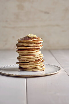Stack of pancakes topped with butter on white plate