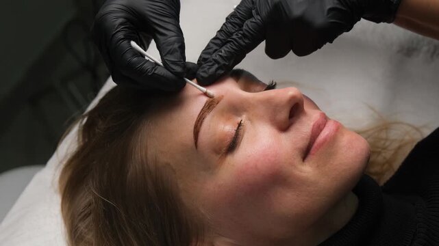 Professional beautician applying henna tint to a client's eyebrows in a cosmetic beauty salon