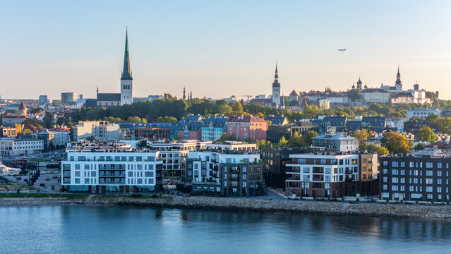 Aerial view of Tallinn Old Town skyline with St. Olaf's Church spire above modern seafront apartments in Kalaranna at golden hour, Estonia