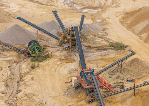 Aerial view of a sand and gravel quarry featuring industrial conveyor belts, sorting machinery, and large piles of extracted materials in Pomeranian Voivodeship, Poland.