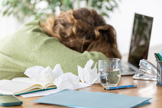 Sick telecommuter lying slumped on the table while teleworking with tissues in autumn