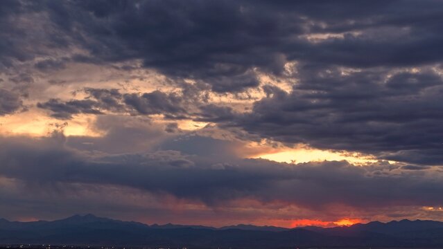 Aerial view of sunset over the horizon with dramatic dark clouds and a glowing orange sky above the distant mountains in Greeley, Colorado, United States.