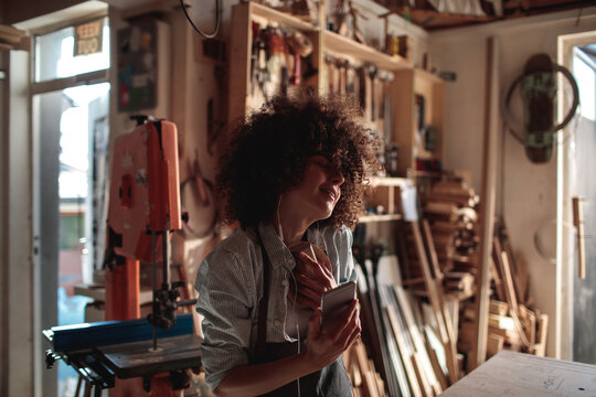 Woman singing with earbuds and smartphone in woodshop