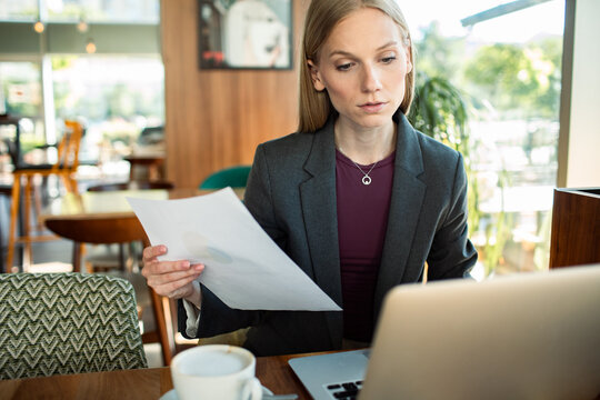 Businesswoman reviewing document while working on laptop in cafe