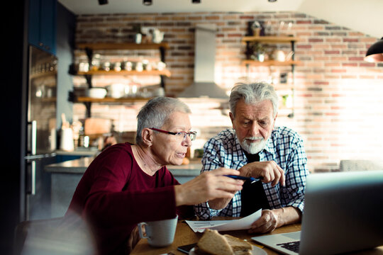 Senior couple reviewing paperwork on laptop at kitchen table