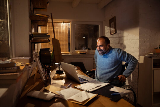 Man in wheelchair working on laptop at home office at night