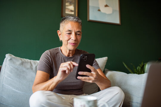 Older woman using smartphone on sofa at home