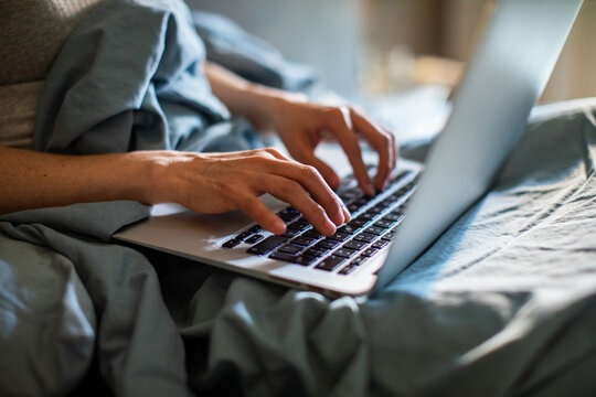 Hands typing on laptop in bed at home