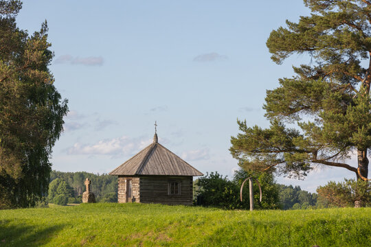 A tranquil summer countryside landscape featuring a small historic wooden chapel on a grassy hill, Savkina Gorka, Russia