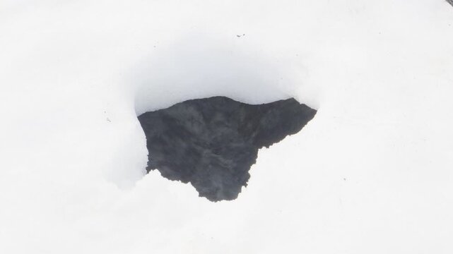 A mesmerizing close-up of a dark, flowing stream seen through a hole in a vast snowfield on Hornstrandir, Iceland. Captures the solitude and remote beauty of this pristine nature reserve.