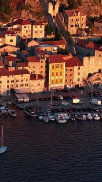 Croatia, aerial footage of a coastal town with old stone houses, red roofs, and boats moored in the harbor at sunset