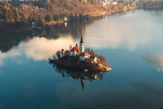 Aerial view of Bled Island with its church and buildings reflected in the calm waters of Lake Bled, surrounded by forests Slovenia.