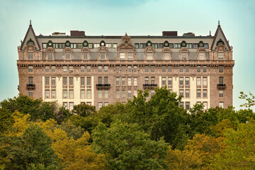 Apartment building at 135 Central Park West in New York City, viewed from Central Park, rises above leafy trees with an ornate stone facade, rows of windows and a steep roof with decorative gables. © Jose Luis Stephens