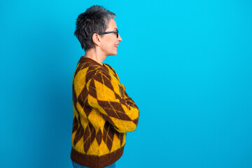 Woman in patterned sweater smiling in profile against blue background, casual senior portrait with short gray hair, glasses and confident relaxed pose © deagreez