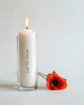 Lit white memorial candle with lest we forget text and red poppy flower isolated on white background.