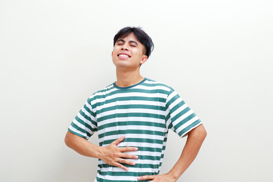 Young Southeast Asian man touching his stomach with a satisfied smile after eating a full meal against a plain studio background, suitable for food, health, and lifestyle advertising
