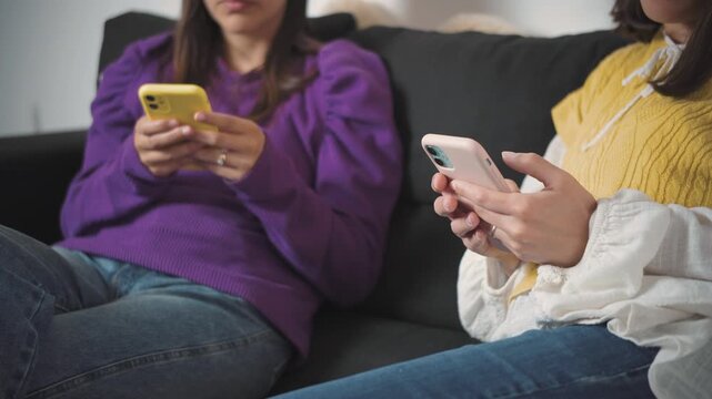 Close-up of two anonymous young women's hands using smartphones while sitting together on a sofa. Concept of digital communication, social media, mobile technology, modern lifestyle, and everyday leis