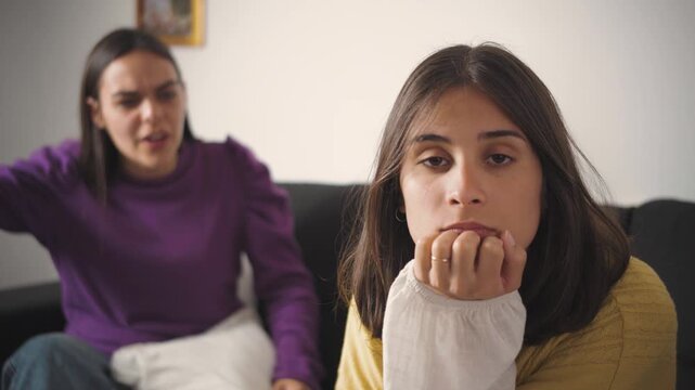 Young Latina woman looking at the camera while ignoring her angry friend beside her during an argument. Concept of friendship conflict, interpersonal tension, emotional distance, communication problem