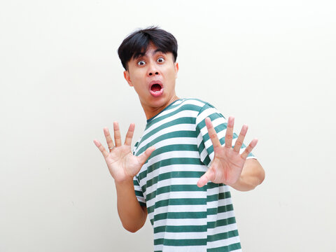 A shocked young Asian man making funny face with raised palms stop gesture against studio background for funny reaction and rejection campaign advertisement banner.