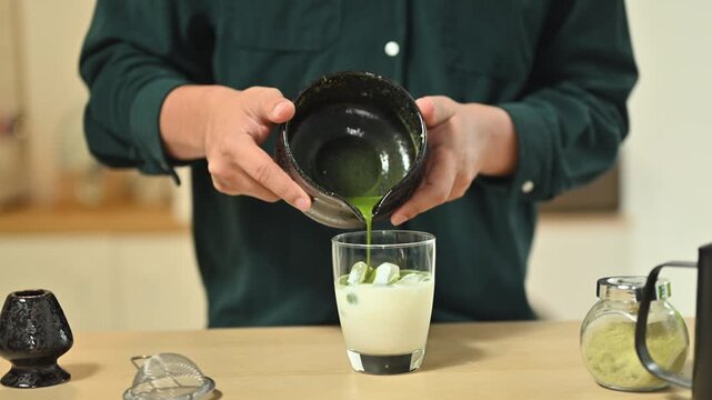 Cropped shot man pouring matcha into iced milk to make a layered matcha latte