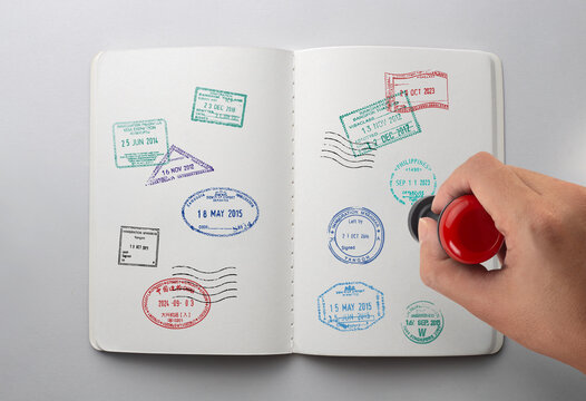 Hand stamping rubber immigration visa stamps into open travel journal notebook top view isolated on white background