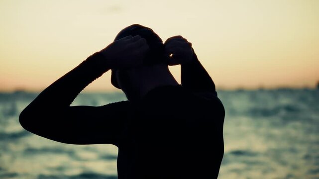 Swimmer Adjusting Goggles While Standing By Ocean At Sunset