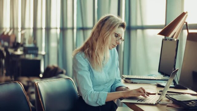 Office Worker Typing On Laptop While Sitting At Desk With Computer Monitors