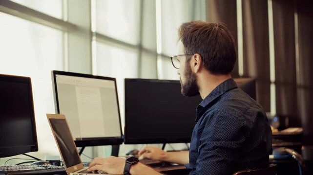 Programmer Typing On Laptop While Working With Multiple Monitors In Modern Office 