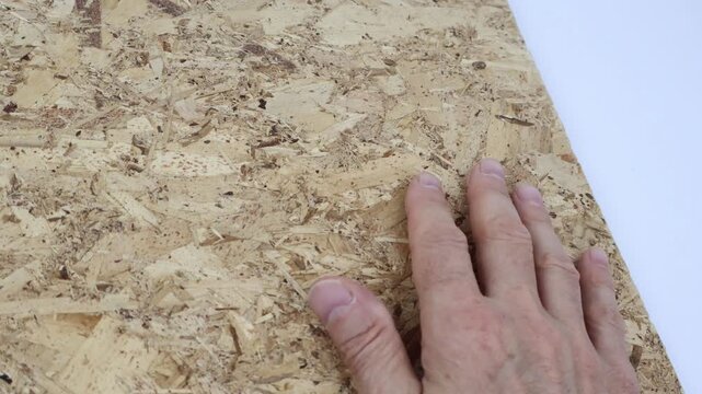 A man's hand rests on a textured OSB panel, ideal as a construction-themed background.