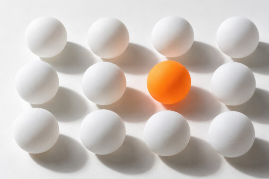 An orange sphere stands out among white spheres arranged in rows on a bright surface, creating a visual concept of uniqueness and individuality.