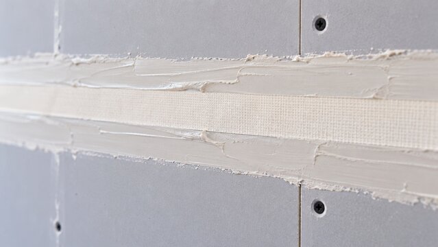 Close-up of residential drywall finishing showing paper joint tape embedded smoothly in fresh joint compound along panel seam