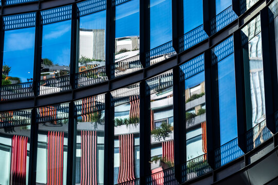 Curved reflective glass facade with blue sky reflections and repeated windows forming modern architecture across a dynamic exterior surface