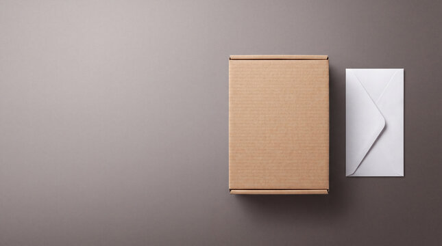 Cardboard mailer box and white envelope on grey background top view