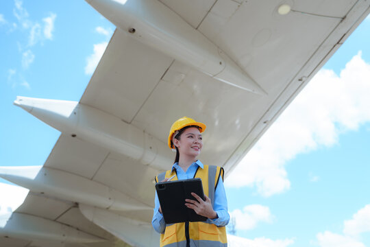 Female aviation engineer inspecting an aircraft wing while holding a tablet outdoors, representing aircraft maintenance, safety inspection, and aerospace technology.