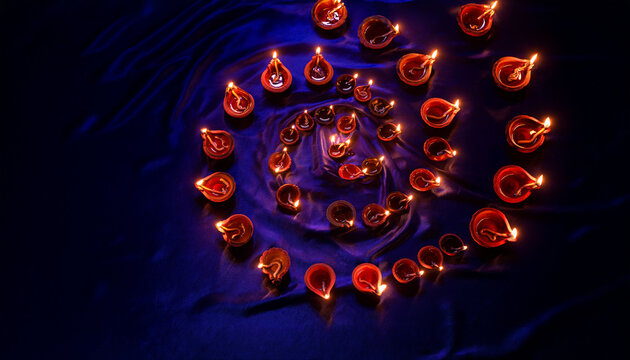Diwali diyas arranged in spiral on blue silk fabric
