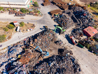 Fototapeta premium Heavy machinery operates at a scrap yard with piles of metal debris in an industrial area during the daytime