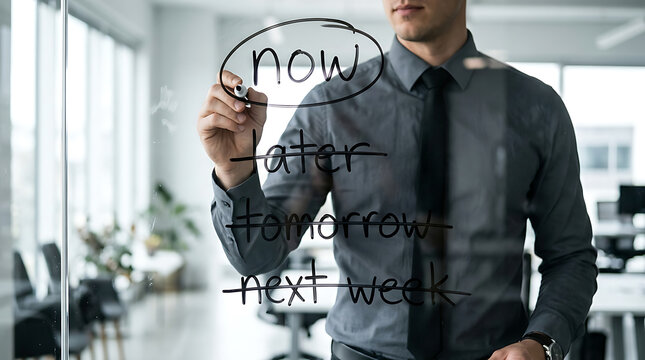 Dedicated professional writing 'now' on glass, illustrating decisive immediate action in office setting