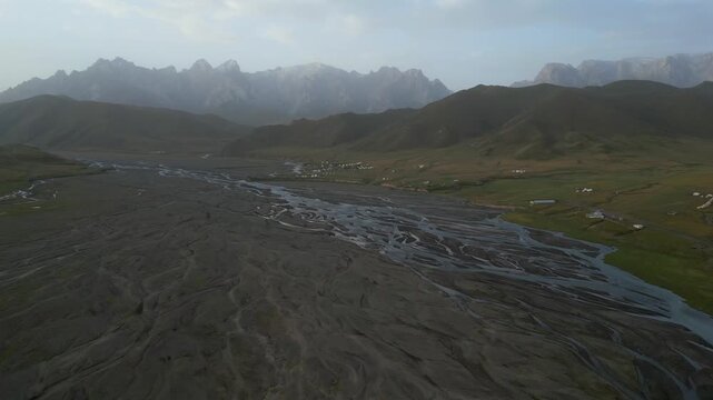 Aerial view of the Kok Kiya Valley in Kyrgyzstan. A braided river flowing through a vast floodplain with green meadows and distant mountains
