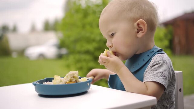 A joyful baby boy munches on nutritious snacks while savoring the fresh summer air on a sunny veranda. This lively scene captures a happy child enjoying healthy outdoor nutrition in nature.