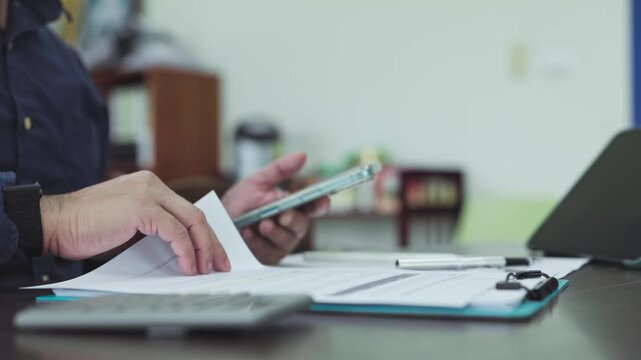 Accountant performs financial audit review paperwork, examining audit balance sheets beside audit calculator at work.