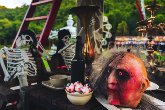 Scary severed witch or zombie head prop on plate with bloody eyeballs prop and potion bottles on wooden table for Halloween display. Concept for Halloween feast, witch potion bar, and spooky party.