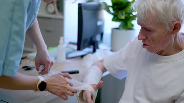 Nurse carefully wraps bandage around fragile wrist of senior patient. Medical staff supports vulnerable elderly man treating osteoporosis in clinic.