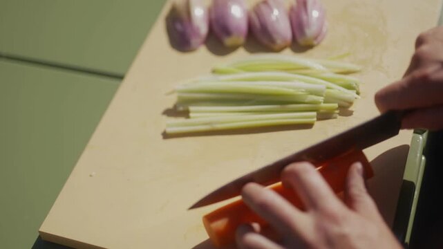 Hands chop carrots and celery on a wooden cutting board