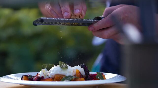 Chef sprinkles parmesan over a gourmet dish in an outdoor kitchen